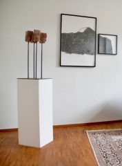 Ein Sockel mit Holzköpfen und zwei Bilder an der Wand als Dekoration im Behandlungsraum.